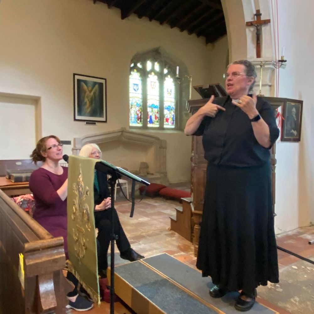 The Revd Hannah Lewis stands speaking and signing in British Sign Language from the front of a church.