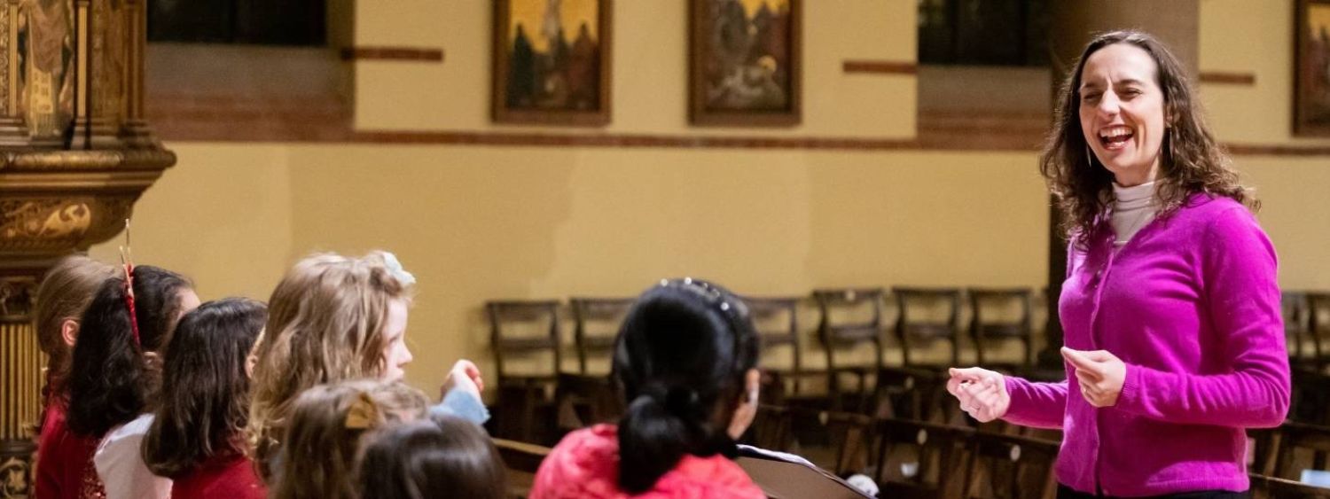 A woman smiles as she leads a children's choir