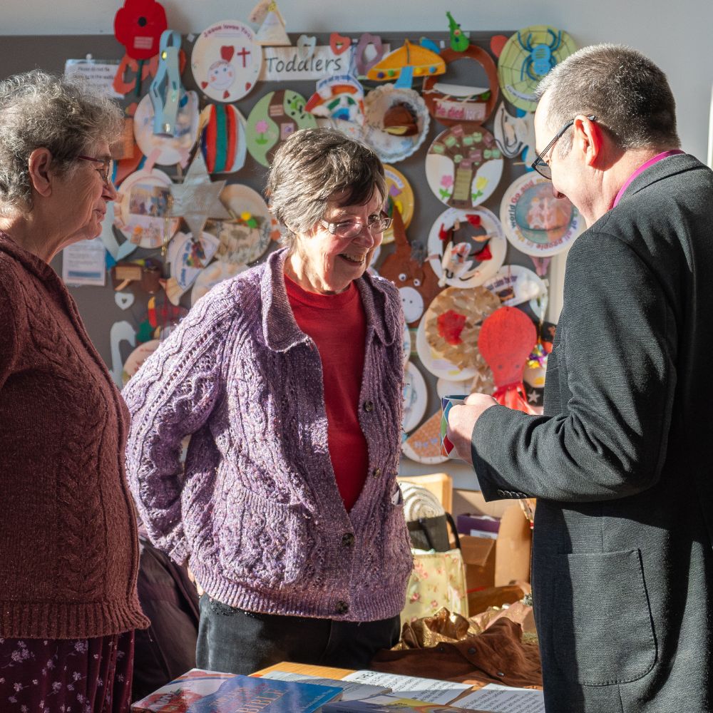 Bishop Gavin speaks to two women in a colourful room