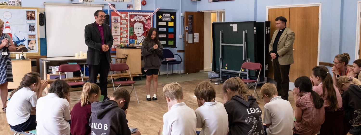 A schoolgirl stands next to Bishop Gavin leading her class in prayer