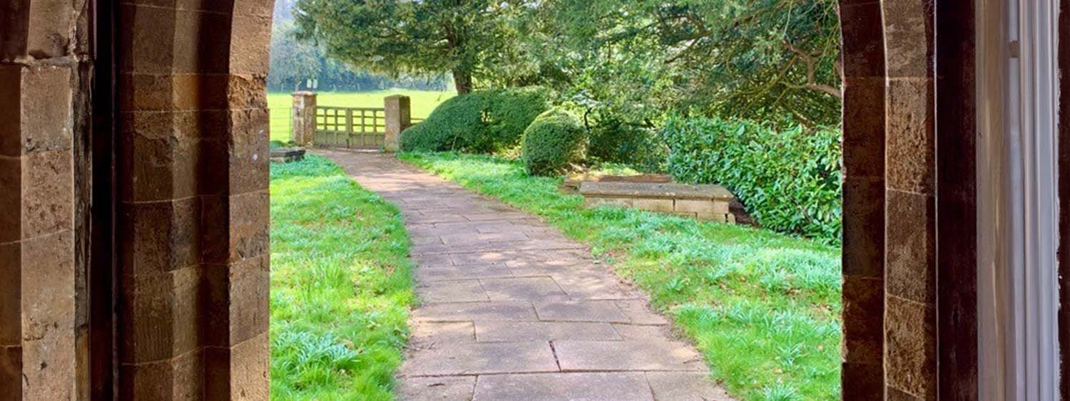 Photograph looking out through church doors onto a garden path