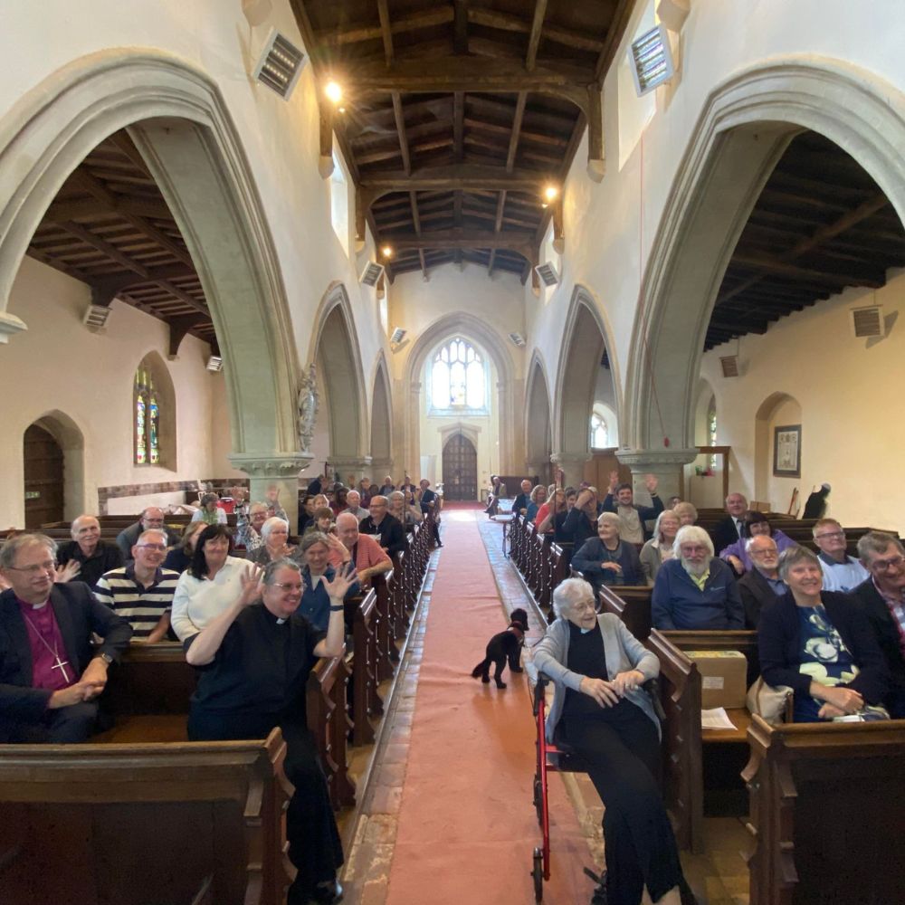 congregation seated in rows wooden pews in a church with arches to the left and right