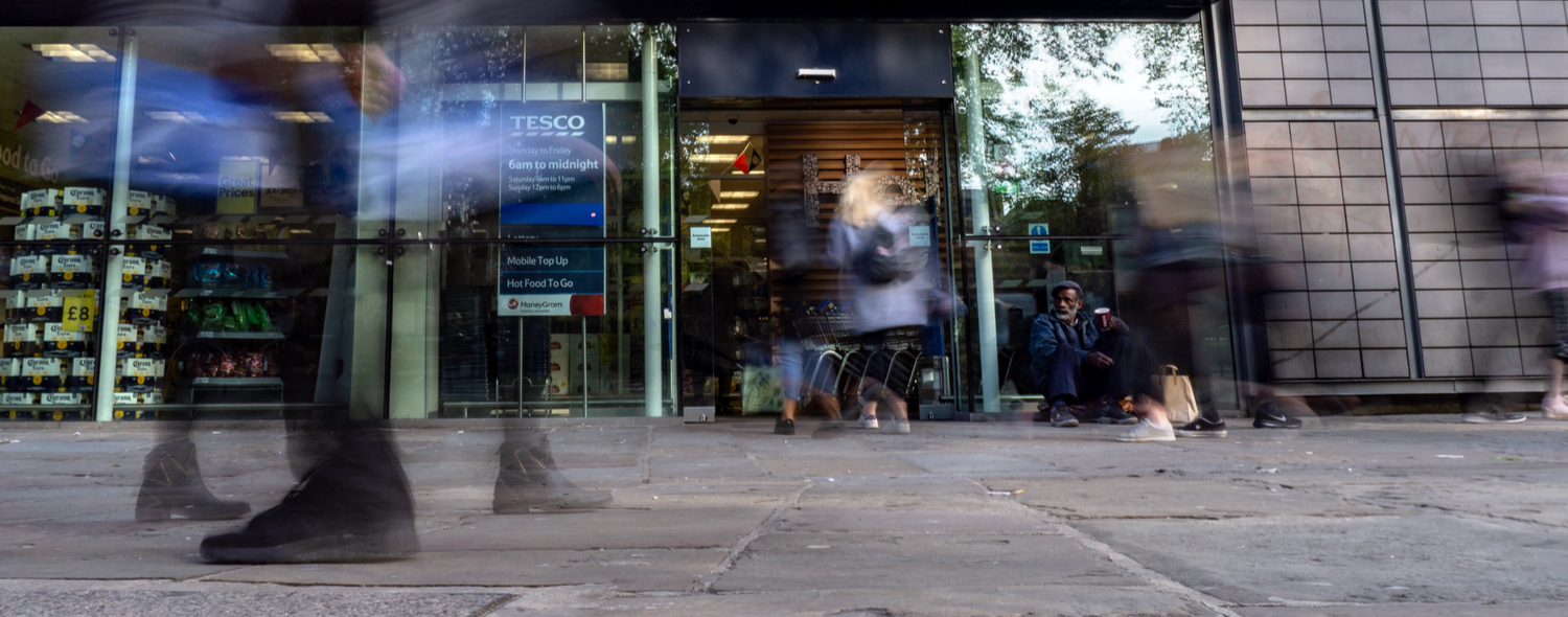 A man sits outside a busy shop as people walk by