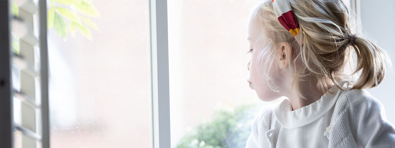 Small girl looks outside of her window at home