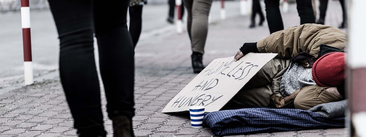 A homeless person lies on the street as people pass them by