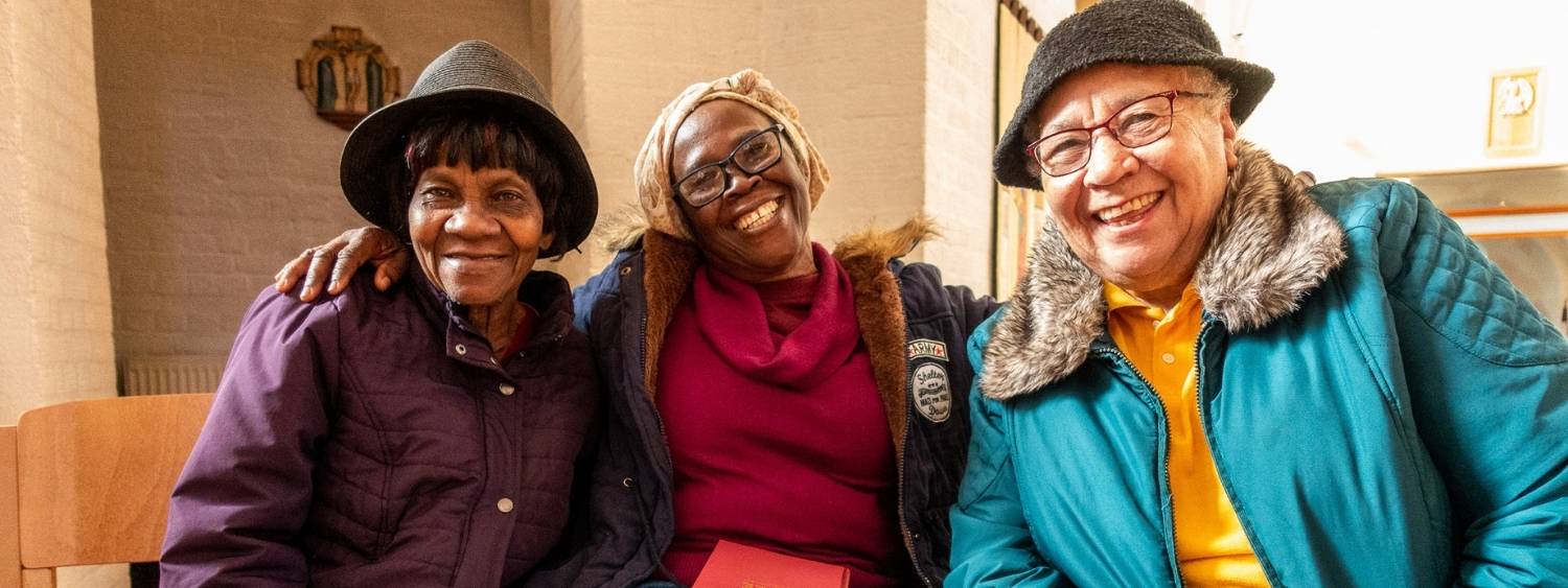 Three women sitting in a row smiling with arms around each other