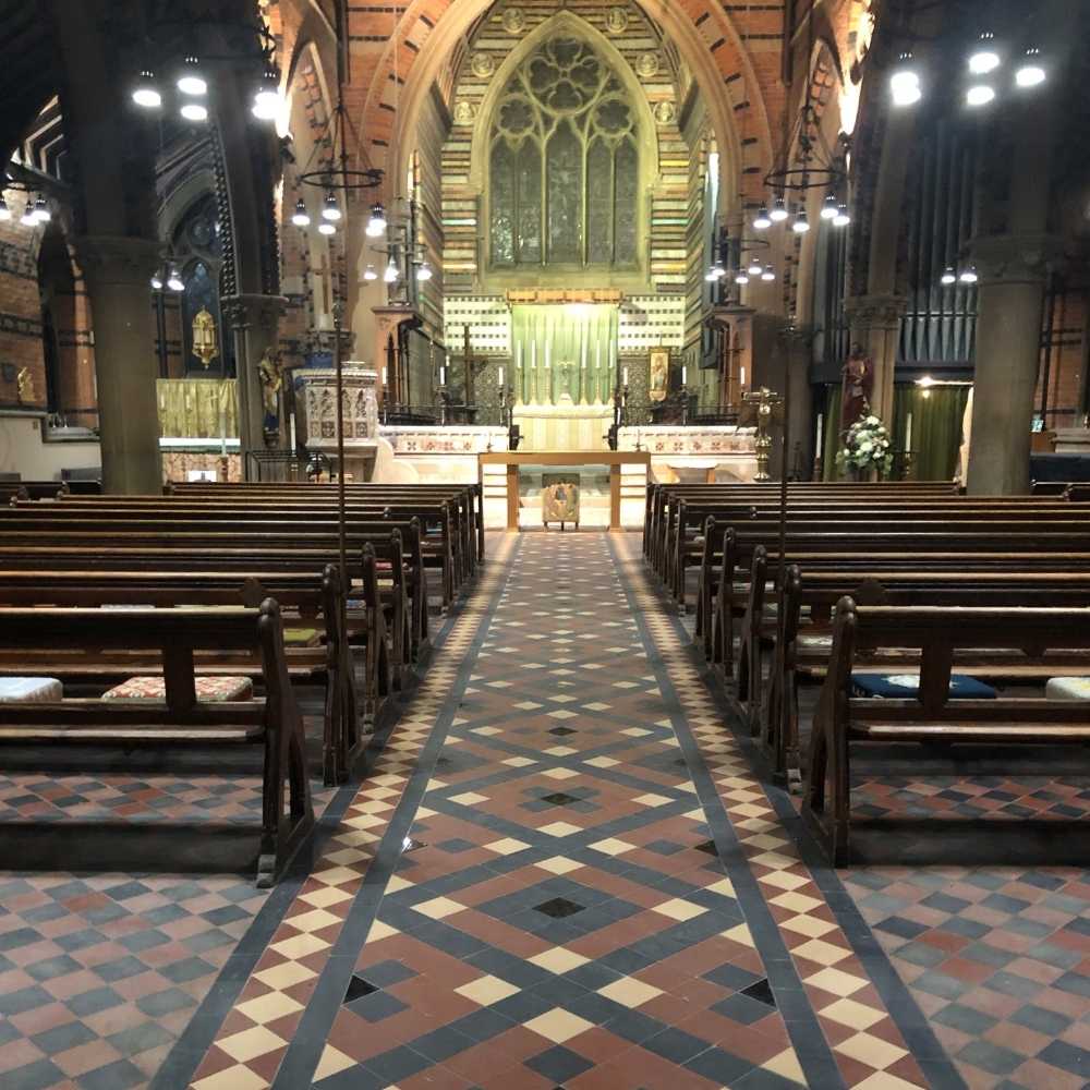 All Saints church looking towards the Altar, pews in rows and multi-coloured tiled floor