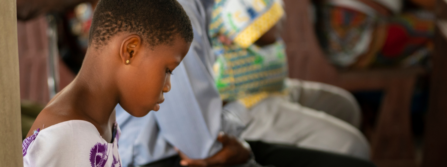 Ho, Ghana - September 16, 2018: A young girl sits on a pew and reads a prayer book during a church service in rural Ghana, West Africa.