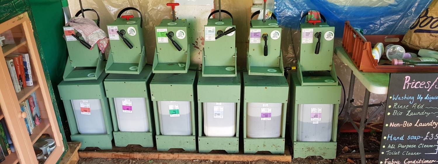 6 green coloured refill tubs filled with soap, detergent and cleaning products sitting inside a garage for people to purchase..