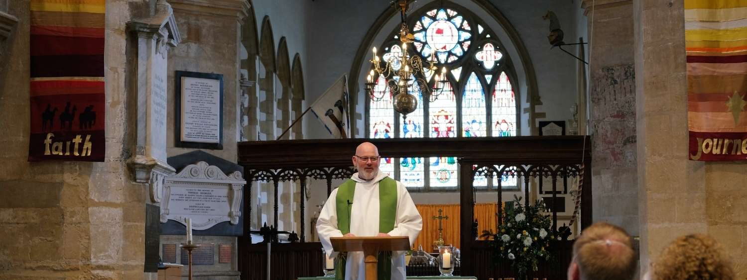 The Revd Mike Reading standing at the front of St Mary's Church, Thame, with stained glass window behind him.