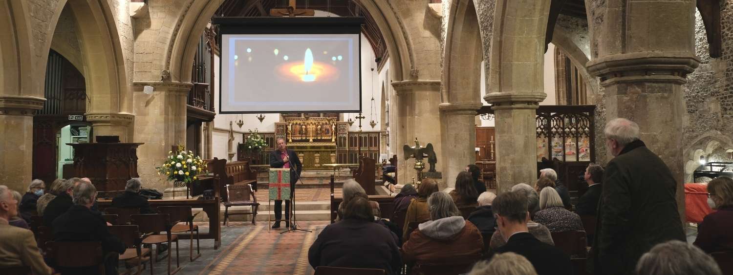 Bishop Steven standing in front of PCC members at St Leonard's Church, Watlington. A gentlemen is standing in his seat asking Bishop Steven a question. 