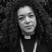 Black and white headshot of the Revd Serena Tajima. Serena wears a rainbow striped lanyard which reads LGBT+ Ally