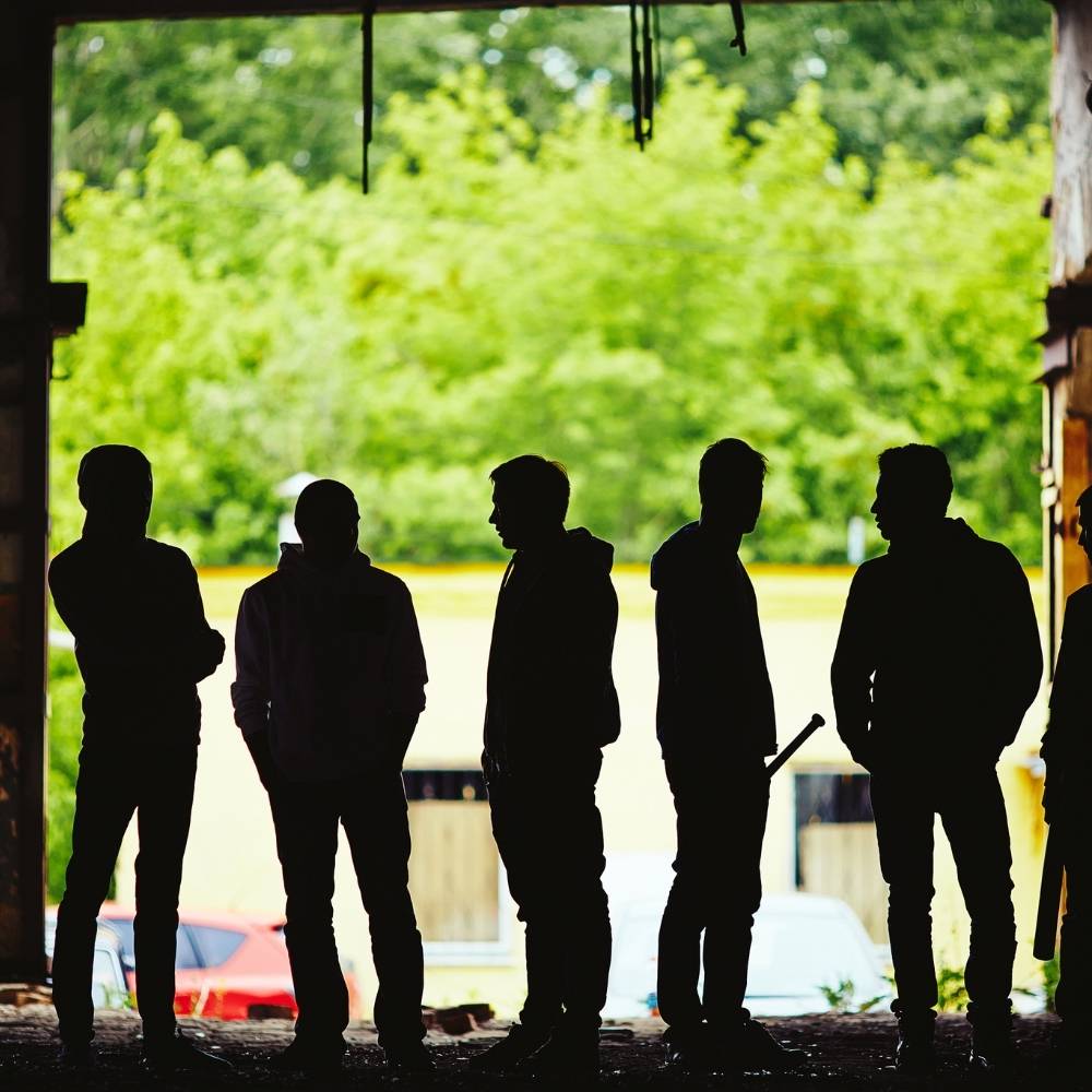 silhouettes of a group of young men standing in a line, some carrying weapons. 