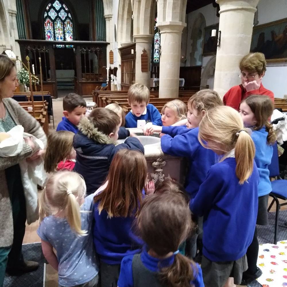 Group of primary aged children standing round a church font.