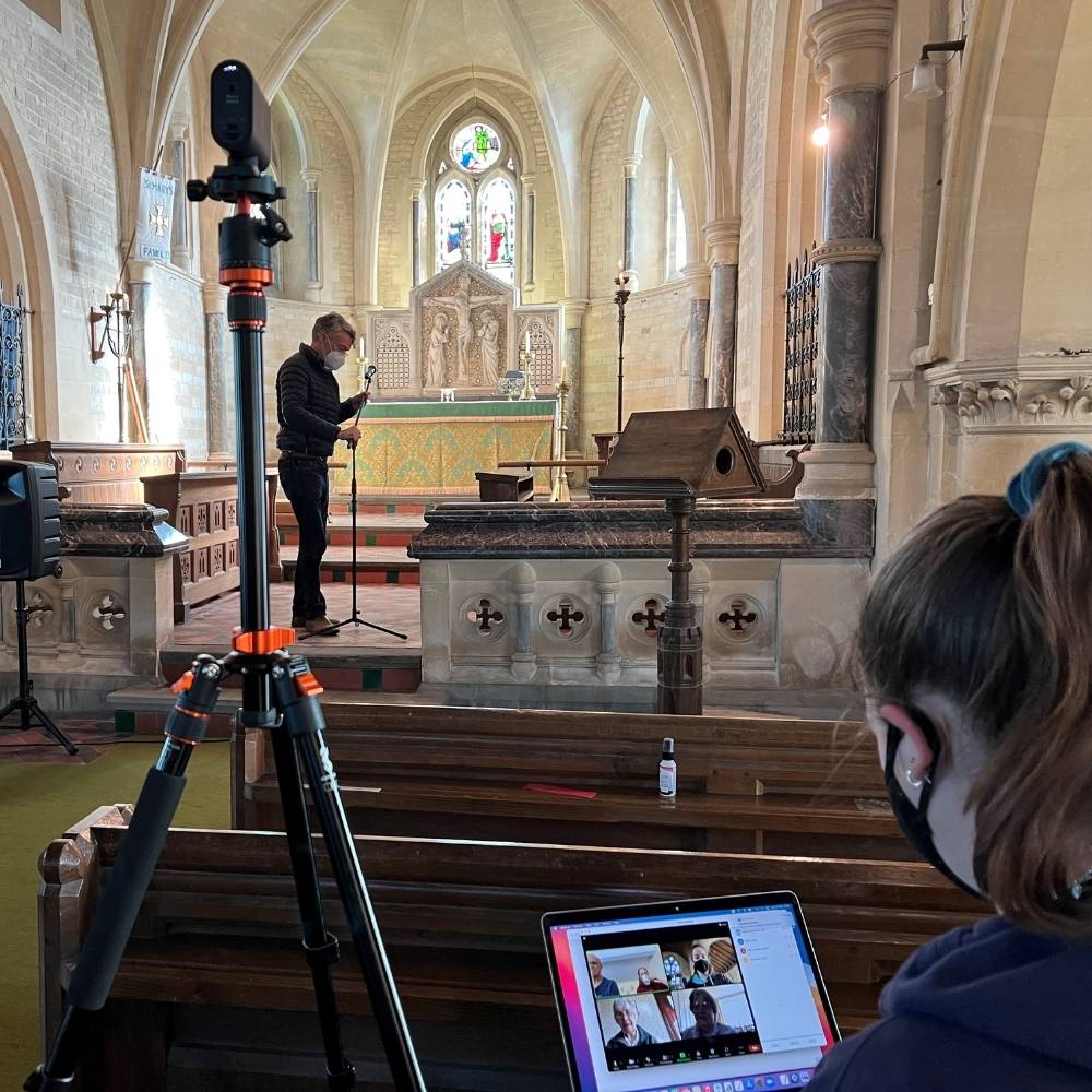 tripod with camera set up for recording church service and young female sat with a Laptop preparing a live stream