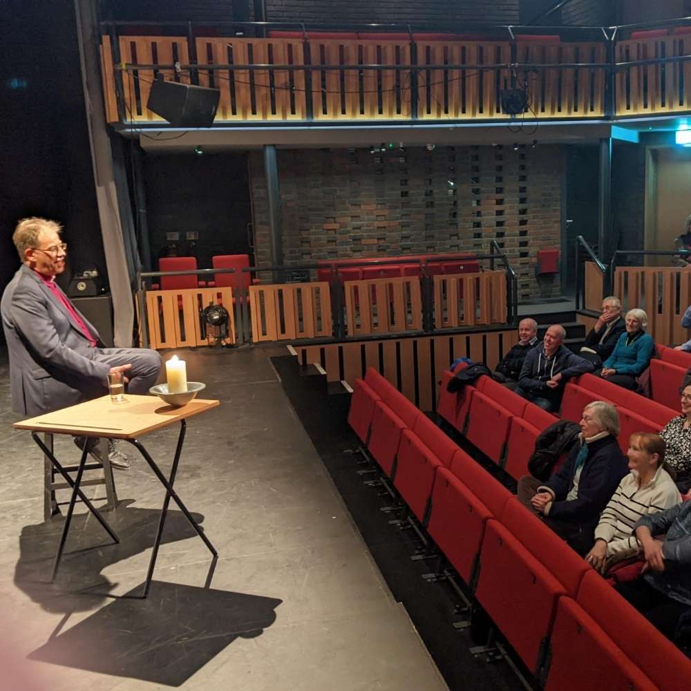 Bishop Steven sitting on a raised stage speaking to PCCs in the Sonning Deanery sitting in red cinema style chairs.