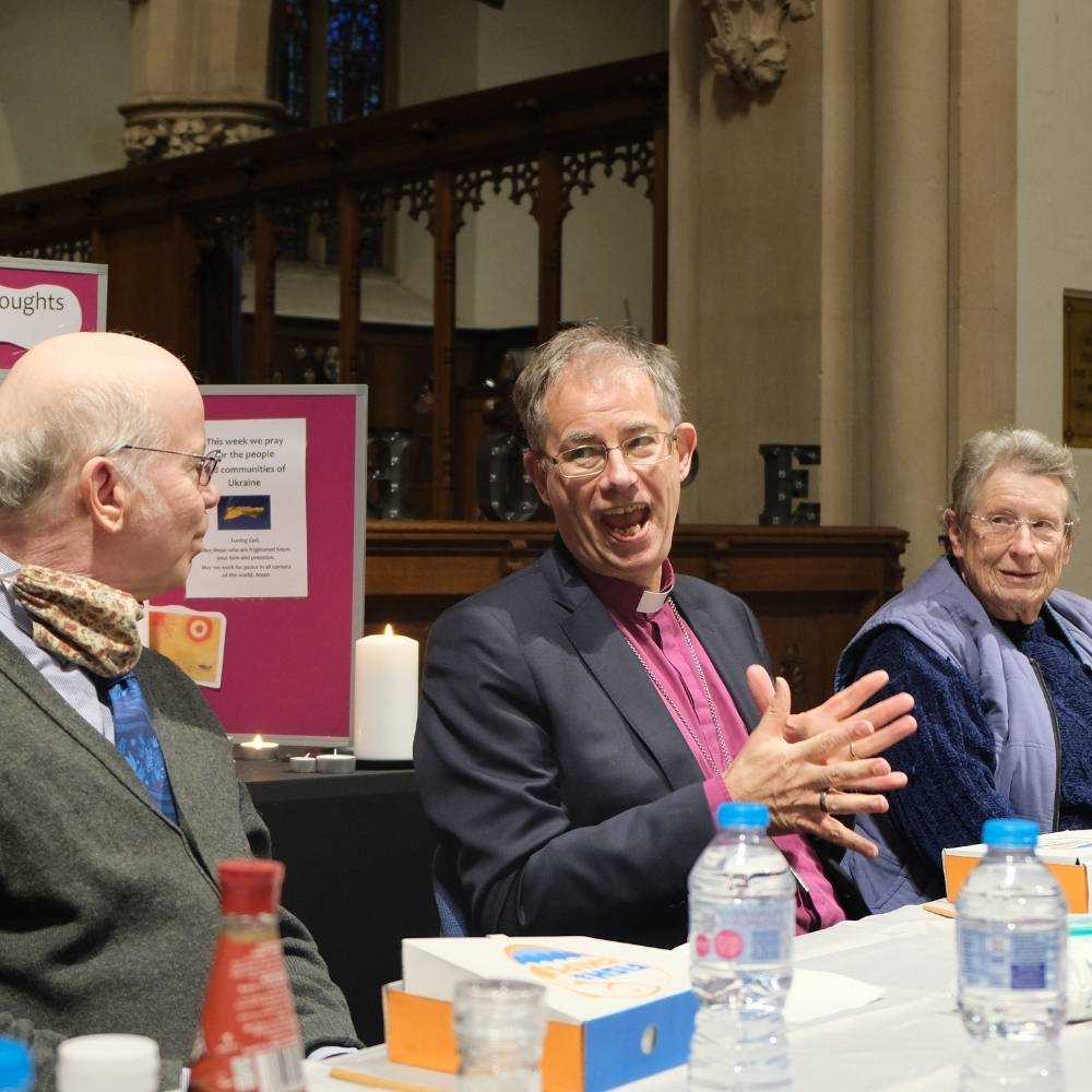 Bishop Steven talking and using his hands sitting at a table in Reading Minster with a male and female Lay Leader sitting on either side.