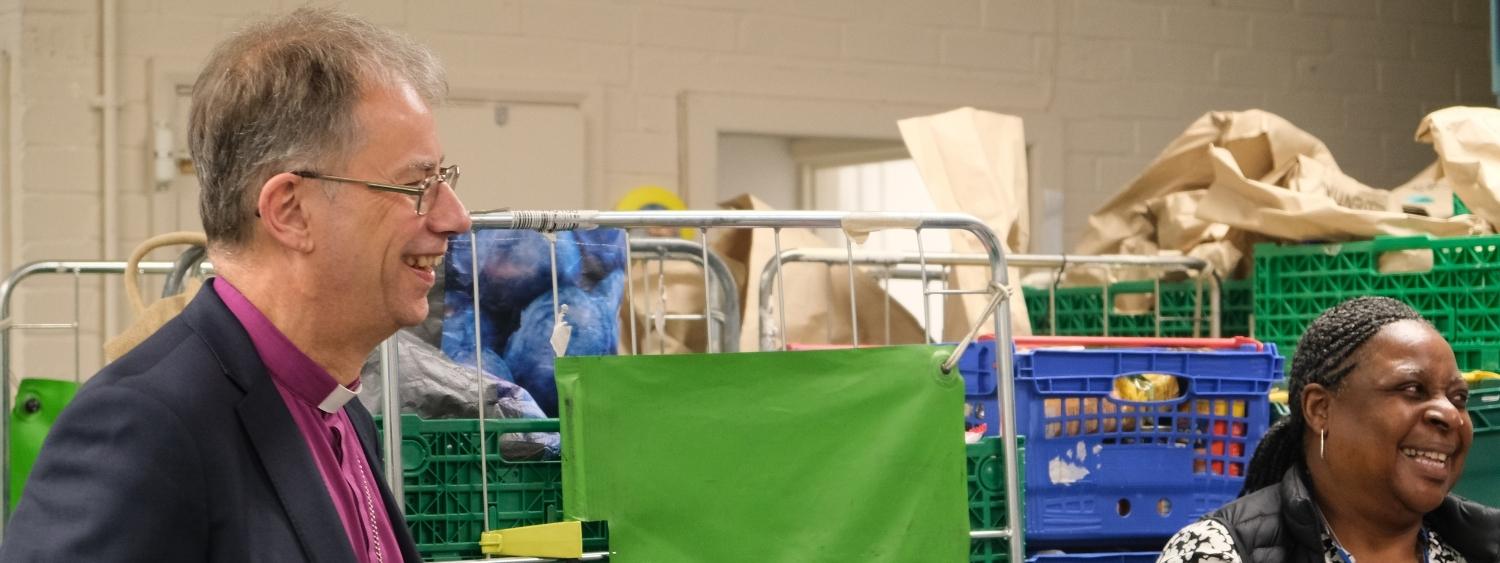 Bishop Steven and Wendy Harris standing smiling and looking to the left of the image in the Reading Food Bank warehouse.