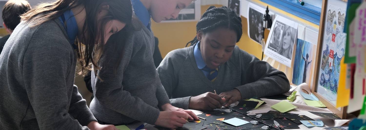 Three young teenage girls at Ranelagh School writing prayers and notes at a table in the school Prayer Room.