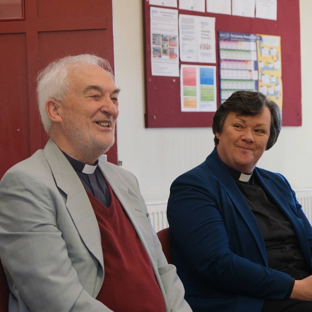 Archdeacon Judy and a clergy person sitting smiling.