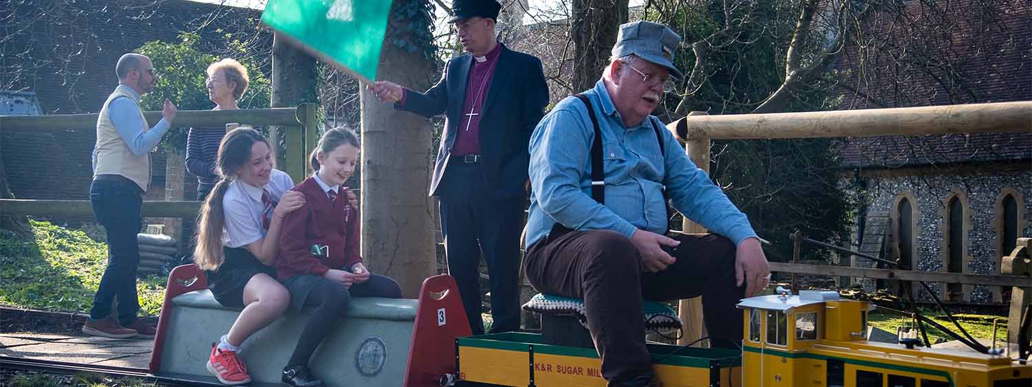 Donning a train driver's cap and holding a green flag, Bishop Steven waves the children off as they have their turn on the trains. 