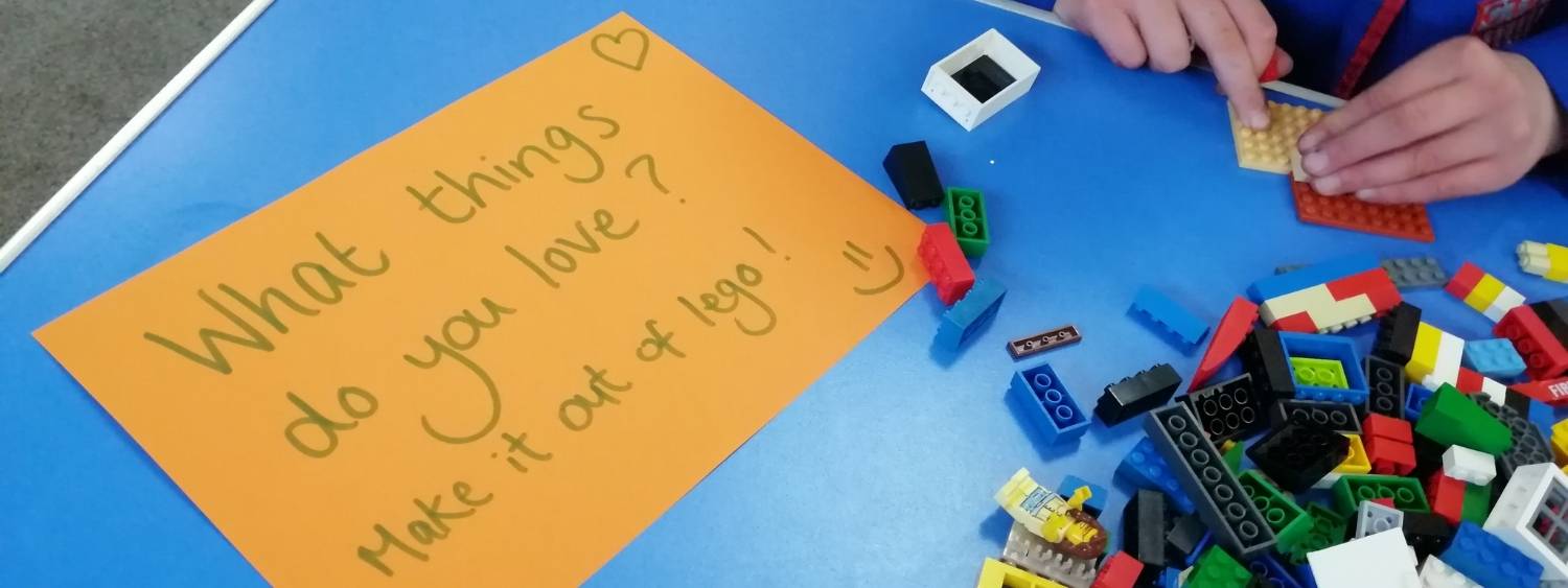 paper on a blue plastic table and a pile of lego pieces reads "What things do you love? make it out of lego!"