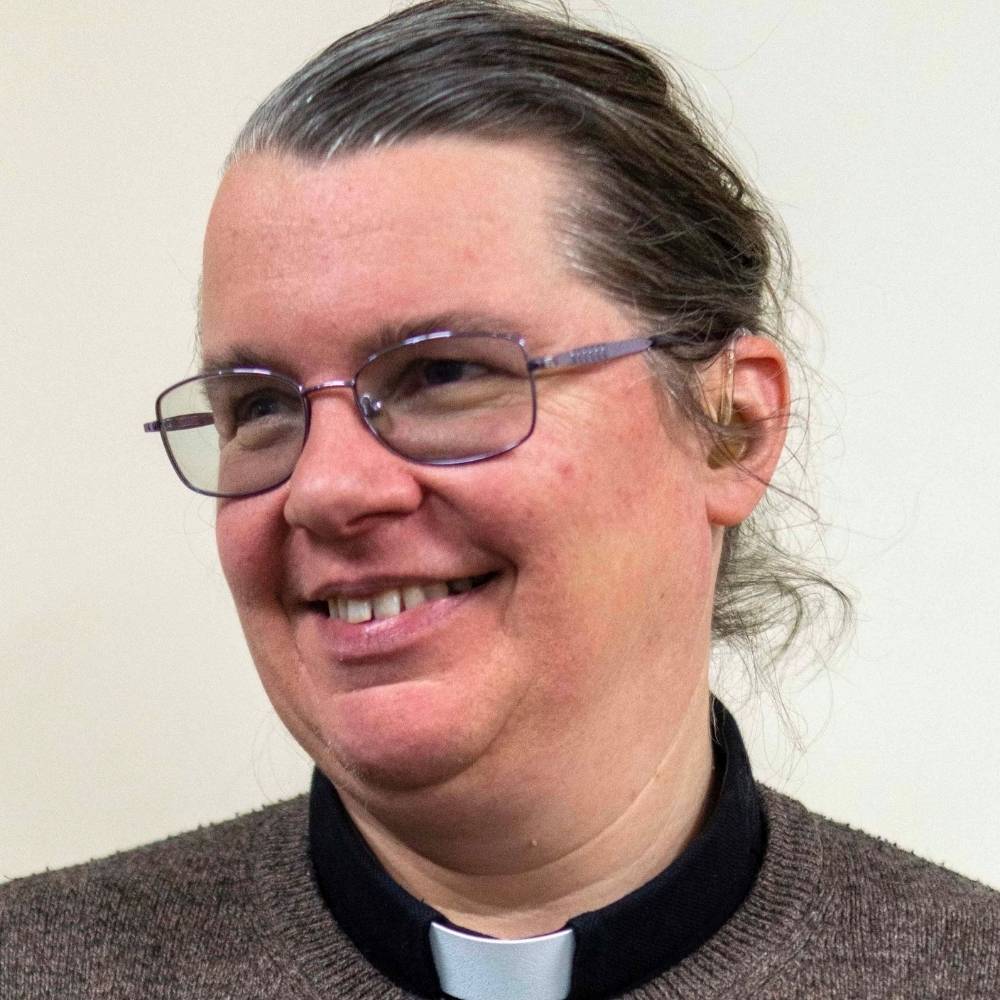 The Revd Dr Hannah Lewis smiling and looking away from the camera, wearing a black clerical shirt and collar.