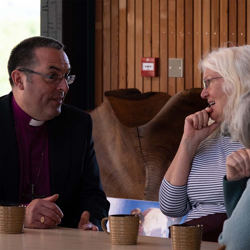 Bishop Gavin speaks to two women over cups of tea