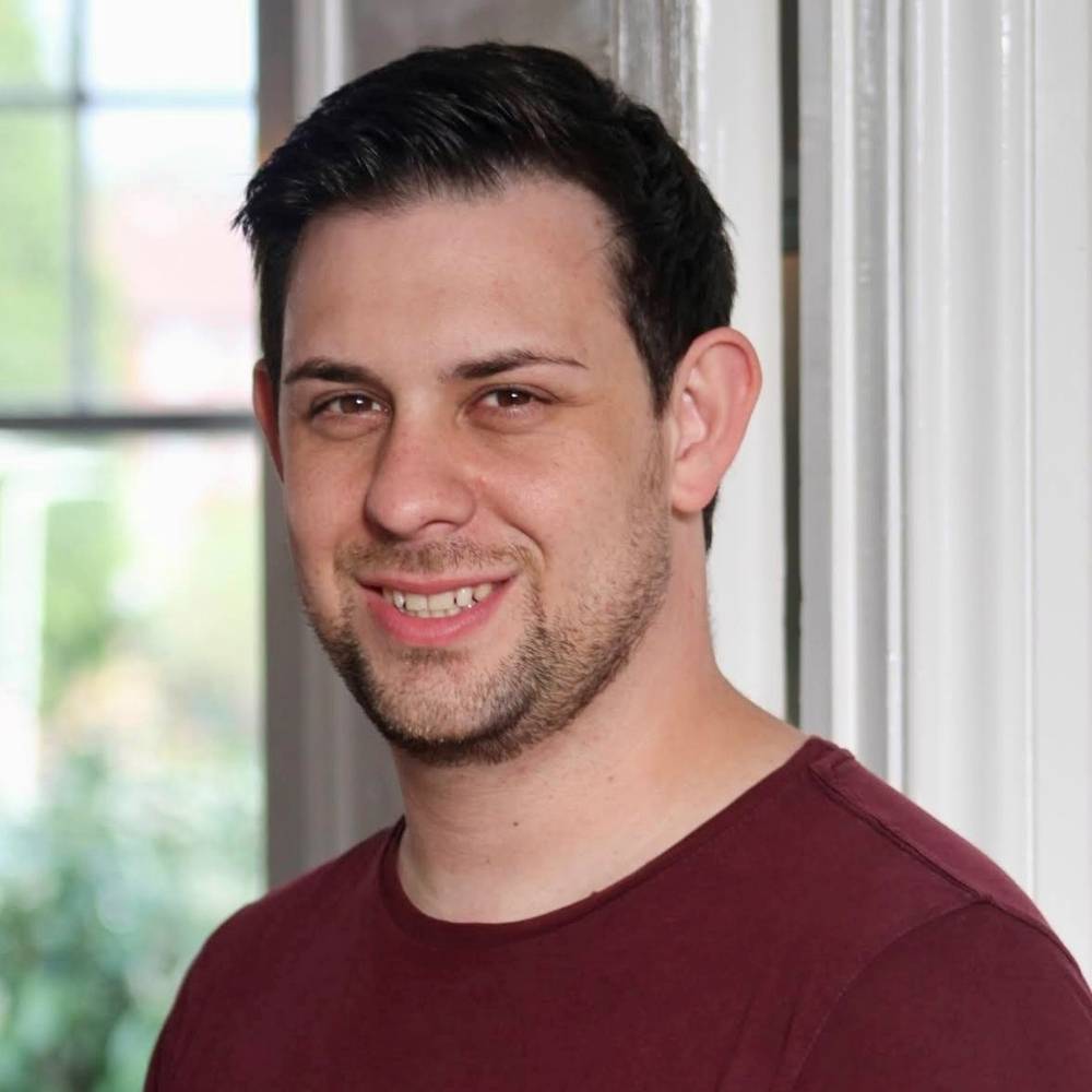 James Wood head and shoulders, he is smiling and wear a dark red round neck jumper.