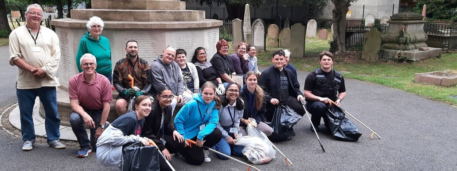 Group of police cadets and church volunteers kneeling in St Marys churchyard with litter picking equipment 