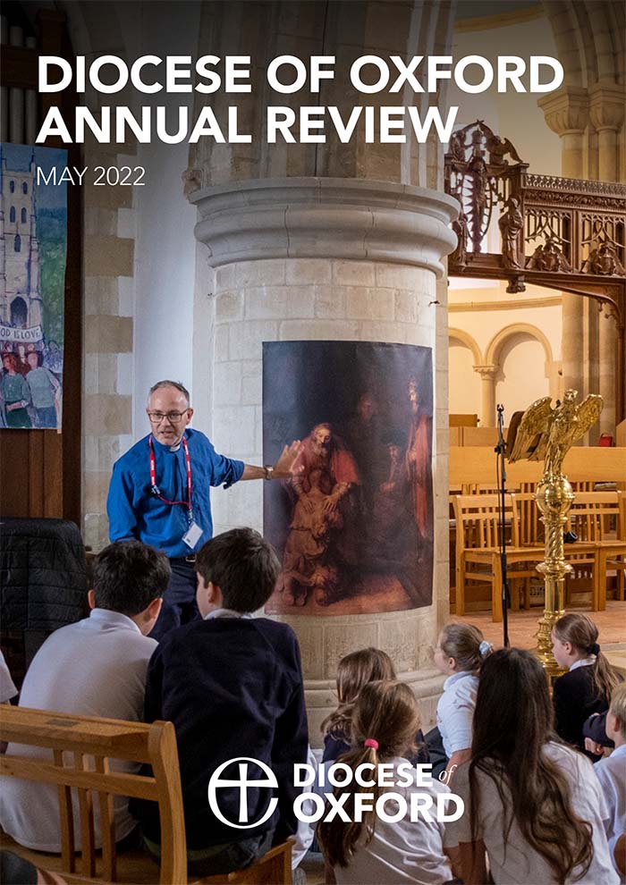2022 Diocese of Oxford Annual Review cover. Photo of Charlie Kerr, schools advisor and chaplain, standing in front of a group of school children. He's gesturing animatedly to a piece of religious art on a church pillar behind him that shows Jesus holding someone who kneels before him.