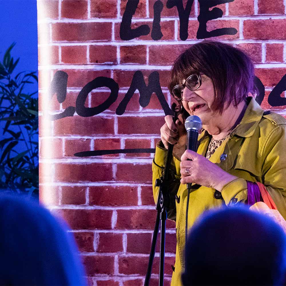 Comedian Barbara Nice leans on her microphone stand onstage