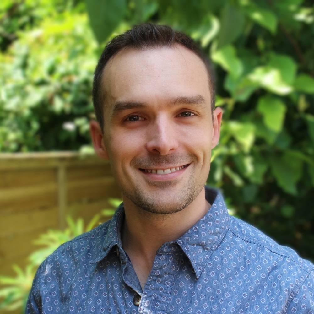 Headshot of Andrew smiling with green trees in the background