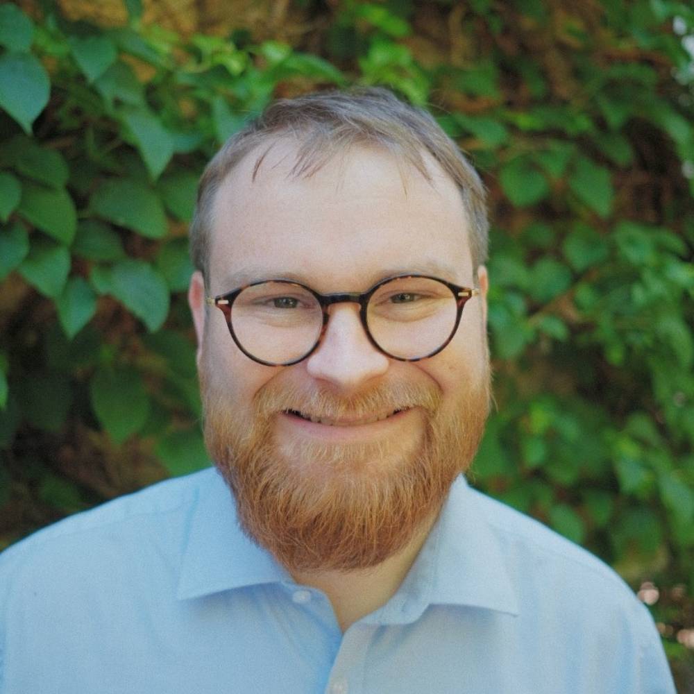 Headshot of Ed smiling with green plants in the background