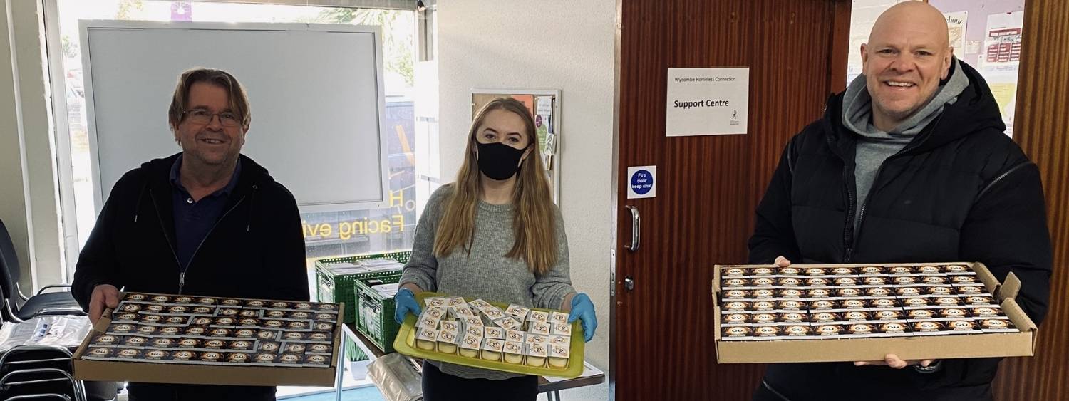 Three volunteers carrying trays of food and smiling