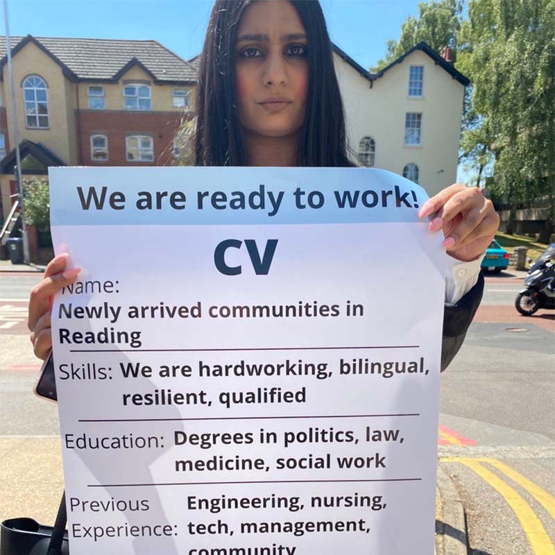 A woman holds a large poster-size CV, encouraging businesses to employ people from newly arrived communities