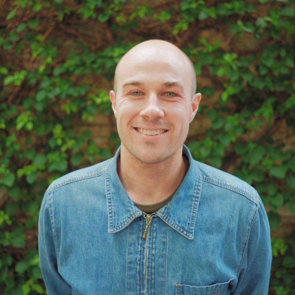 Andrew standing infront of a green leaf wall outside smiling