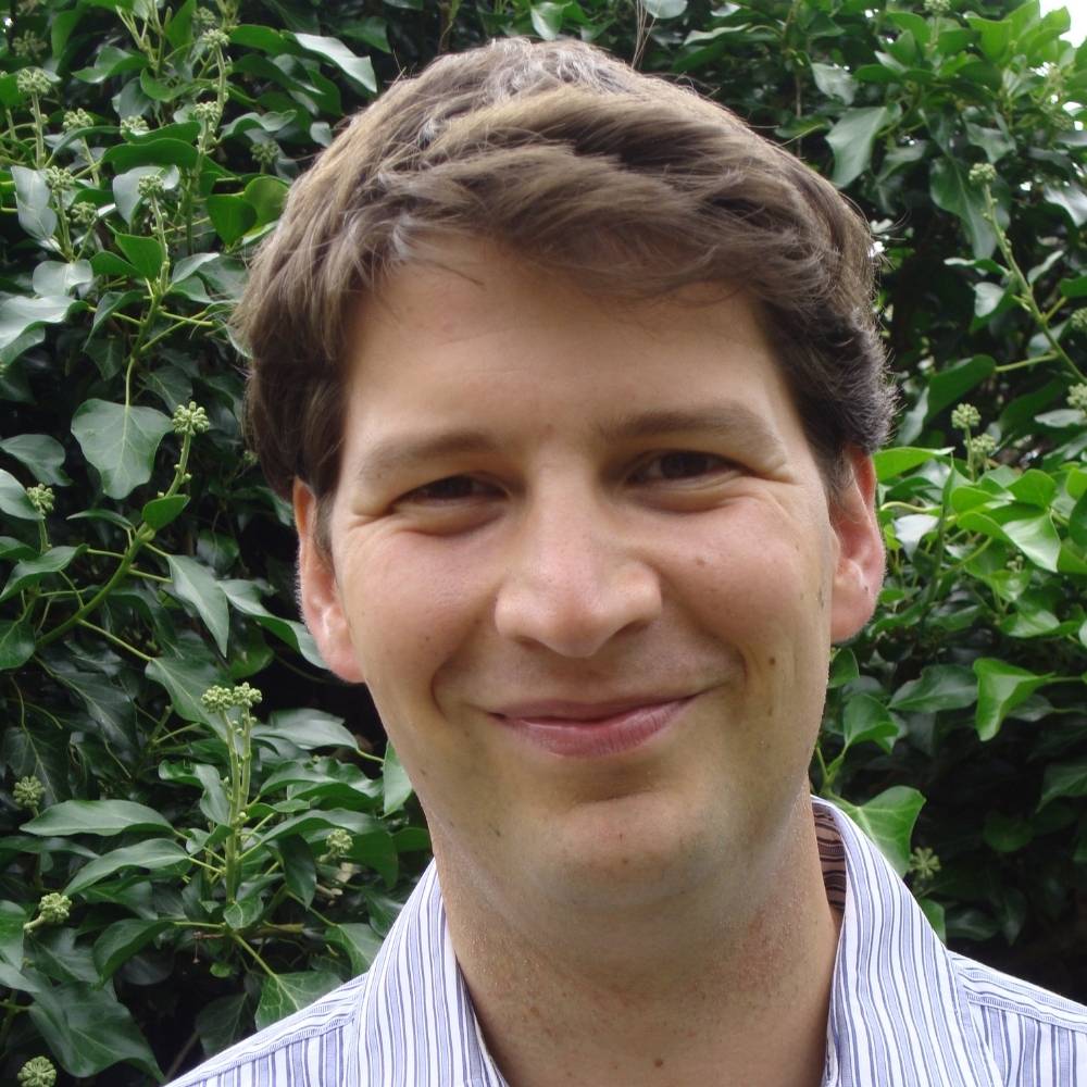 Headshot of Josh standing in front of a green tree smiling