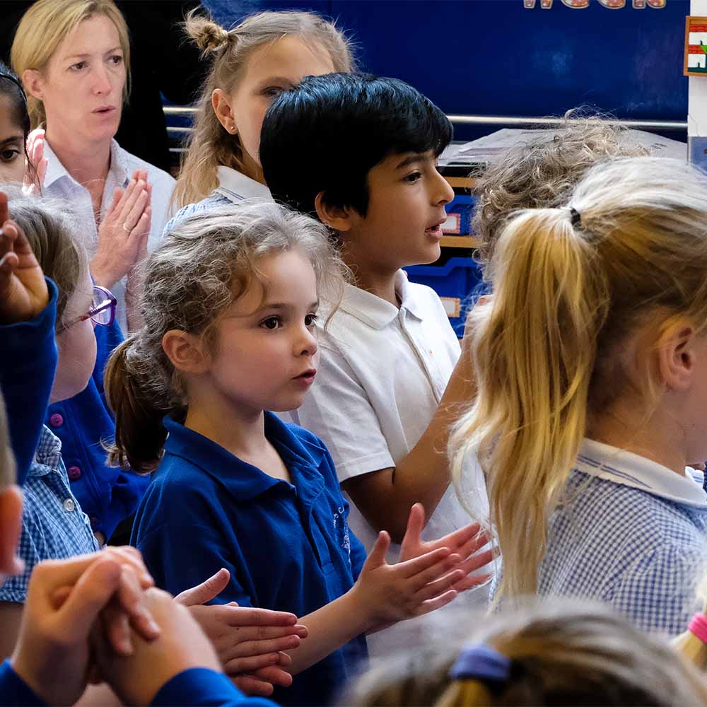 A group of primary school students sing and clap along to a song