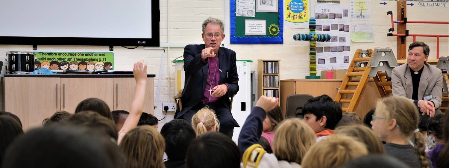 Bishop Steven sits infront of a group of primary school children