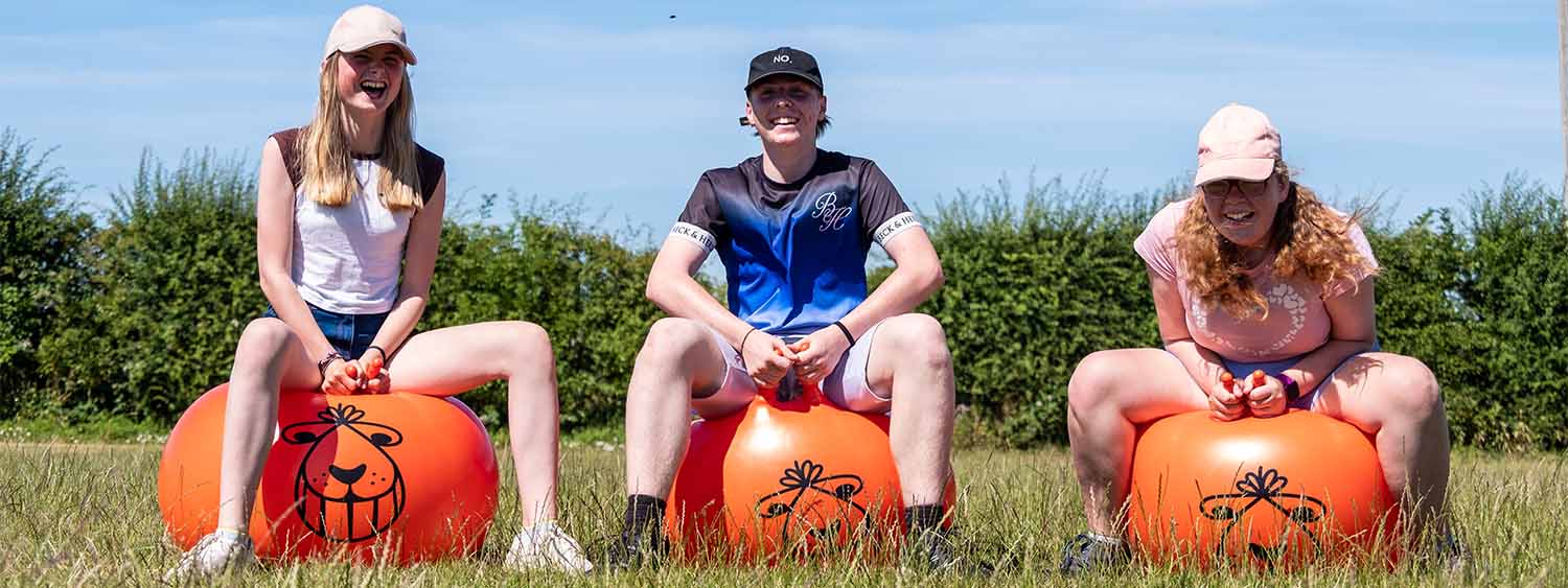 Three young people bounce on orange spacehoppers whilst laughing