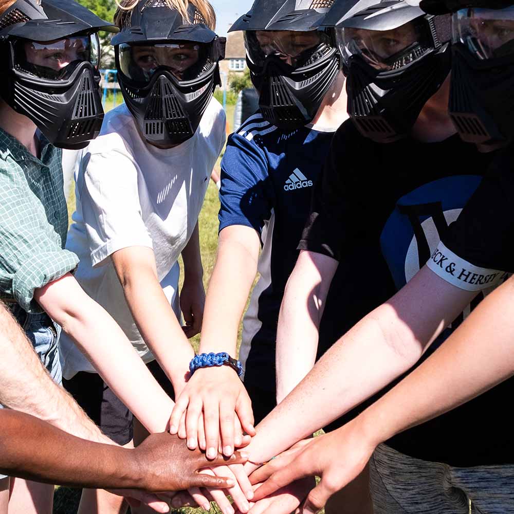A group of young people and adult leaders place their hands in the middle of a team huddle. They are wearing helmets