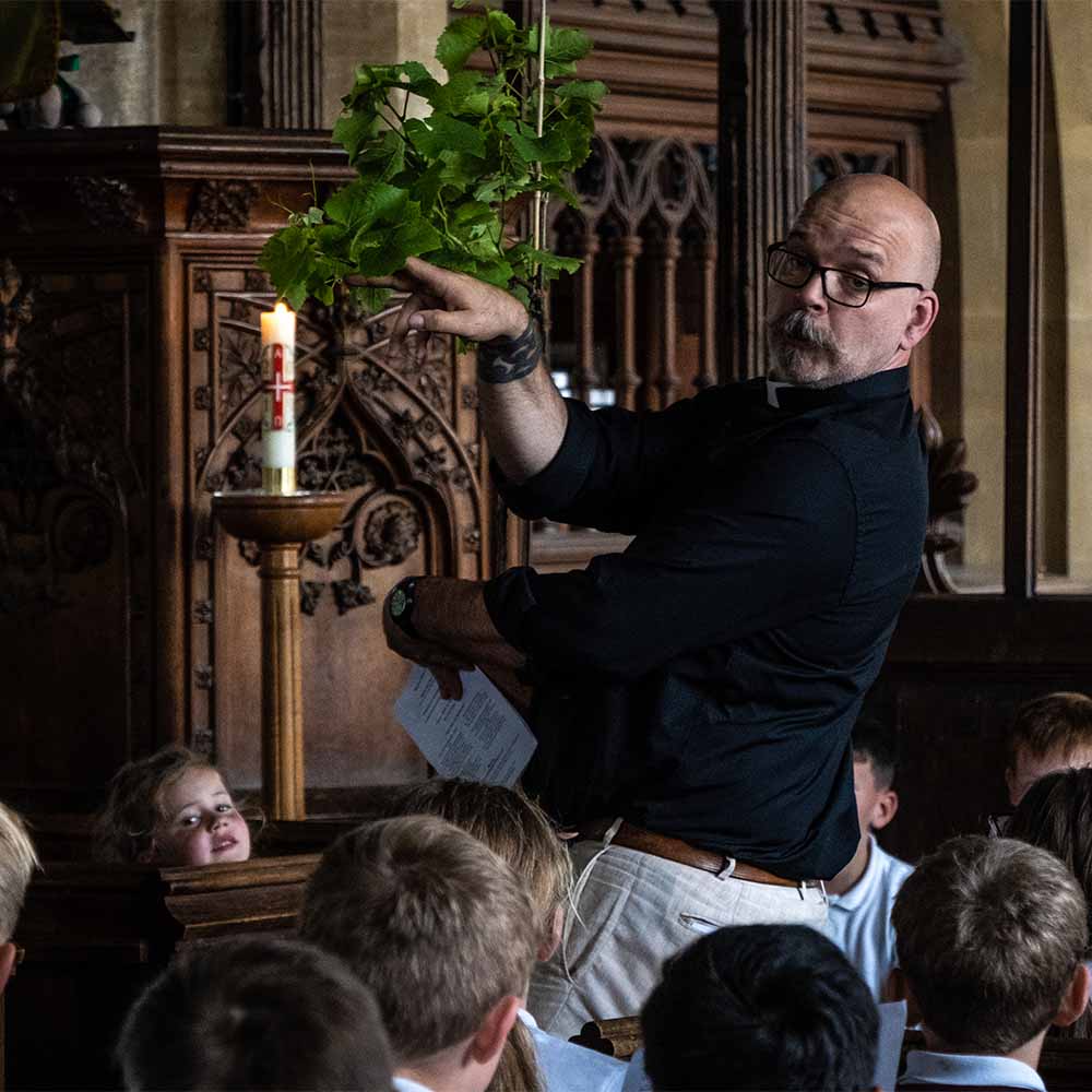 The Revd Mark Nelson animatedly holds up a vine plant during a school service in St James' Church Gt Horwood