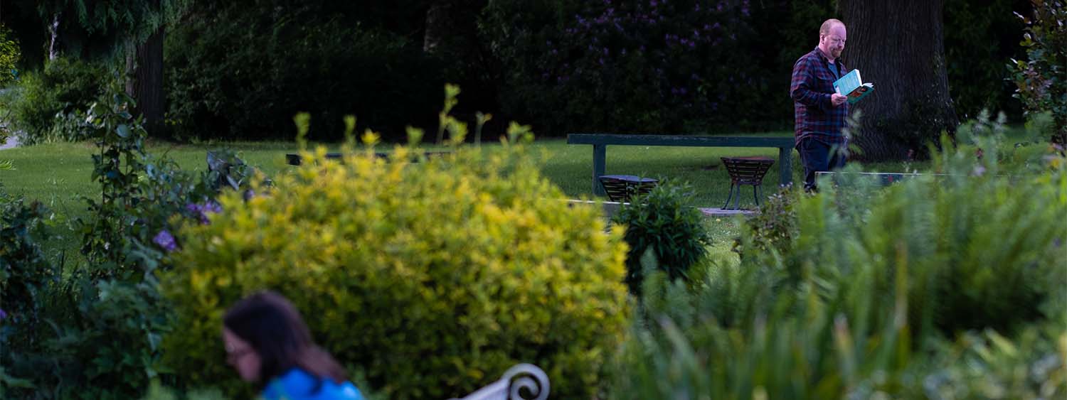 A man walks through a garden reading a book