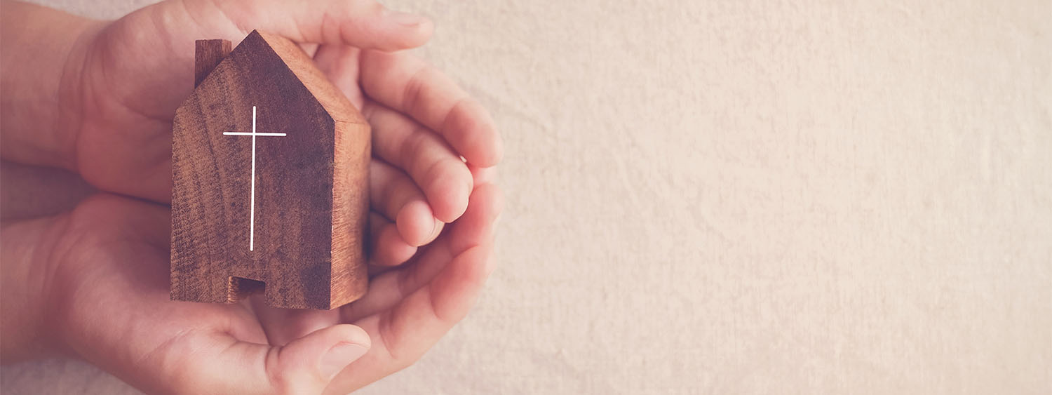 Hands hold a small wooden church.