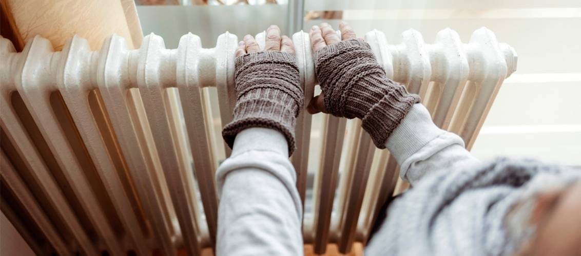 Elderly Man wearing fingerless gloves putting hands on radiator