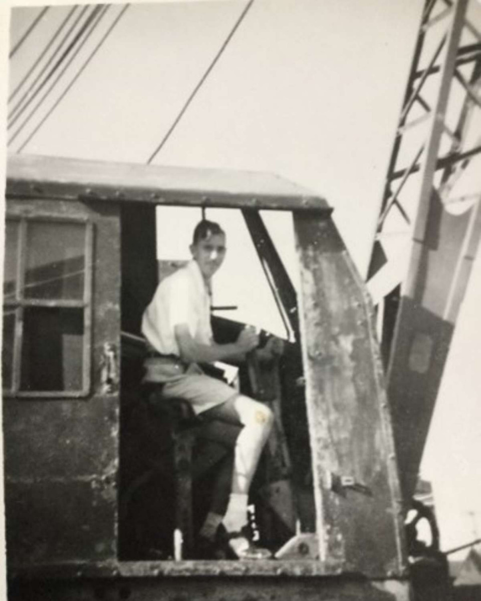 Black and white photo of young Bob Whiteley driving a crane in Belize during the 1950s.