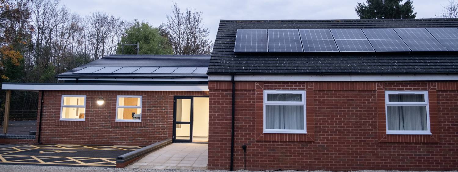 St Andrews Dean court new single storey church building view from the side, a ramp leads up to a side door, solar panels line the roof and there is an accessible parking space at the front of the building.