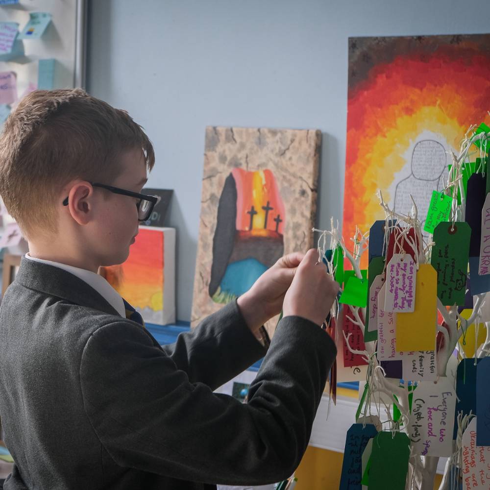 A young teenage boy hangs a hand written note on a prayer tree in school.