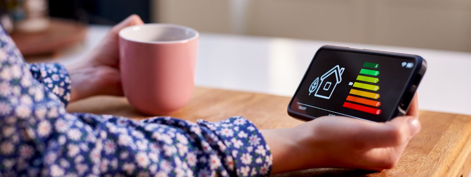 Person holding an in home energy reader displaying energy in one hand and in the other hand a pink mug